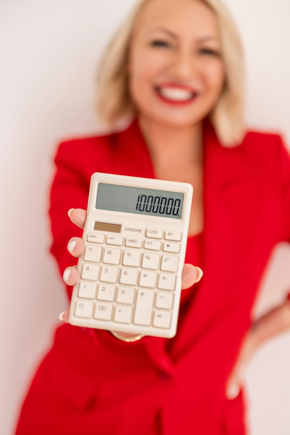 Miranda in a red suit, smiling and holding out a calculator that reads 1,000,000