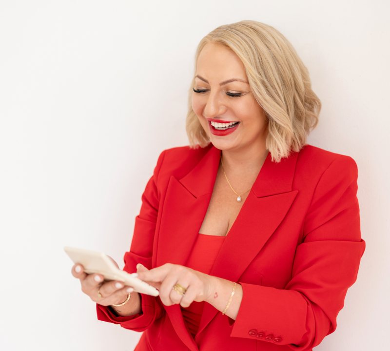 Miranda in a red suit laughing as she taps numbers into a calculator