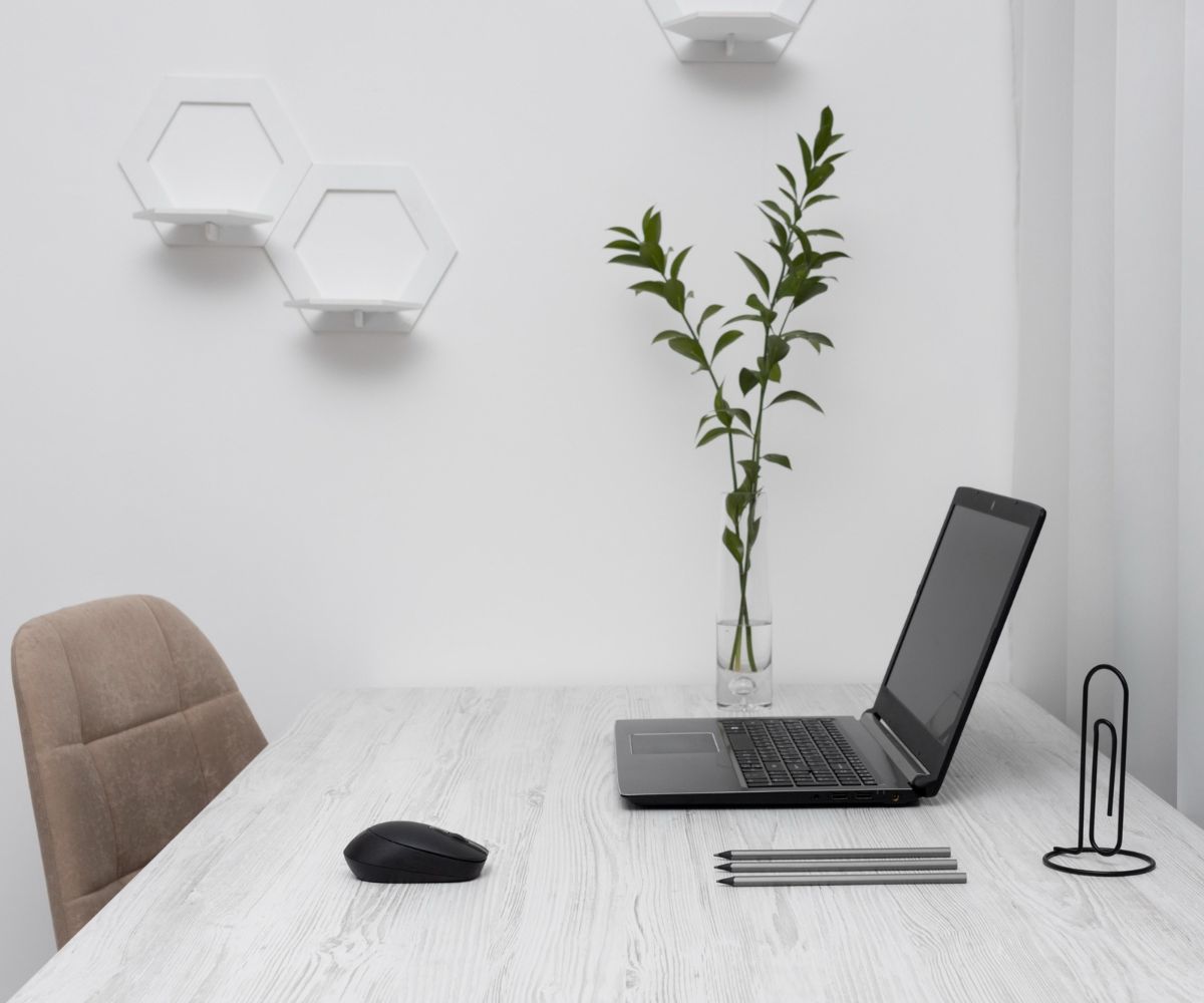 White desk with a brown leather chair to the left black laptop and mouse and green plant sitting on desk.