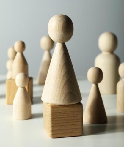 Multiple wooden blocks with round heads and cone-shaped bodies to depict people with two of them standing on square wooden blocks.