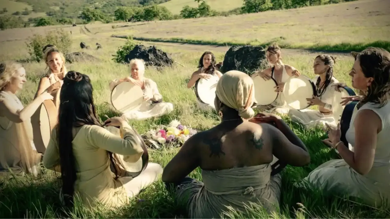 Krista Holland and a group of women frame drummers drumming in a field of grass