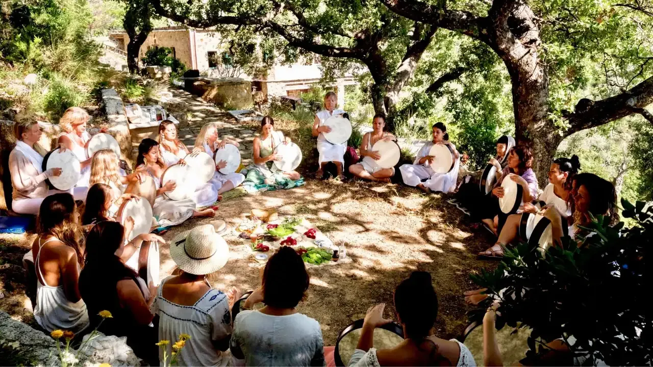 Krista Holland and women sitting in a circle under oak trees in Crete, Greece playing frame drums.