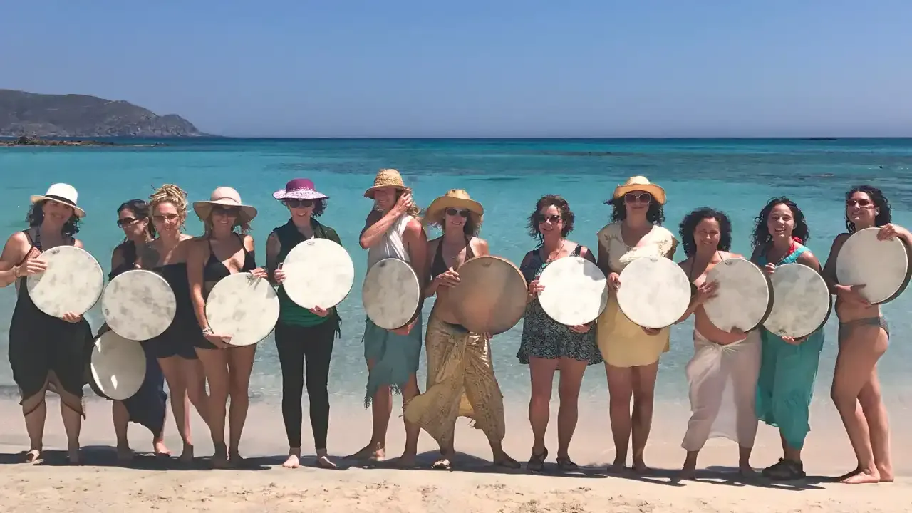 Krista Holland frame drumming on Elafonisi beach on yoga and goddess retreat in Crete, Greece with women holding frame drums