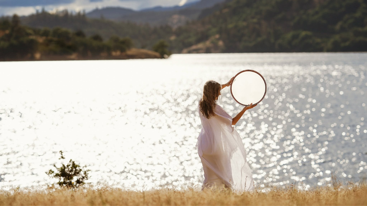 Krista Holland playing a frame drum by a lake in California