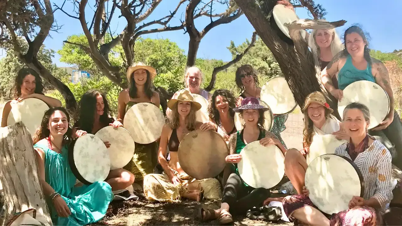 Krista Holland and a group of women sitting under carob trees at Elafonisi beach in Crete, Greece, playing frame drums width="1280" height="720"px