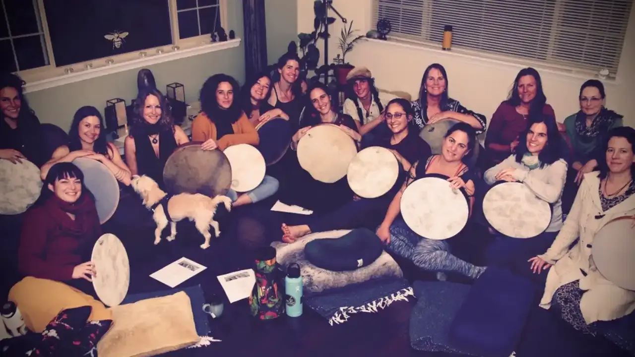 Krista Holland and Liron Meyuhas with a group of women sitting on the floor holding frame drums.