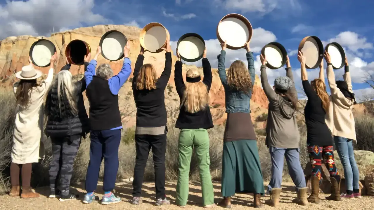 Krista Holland with a group of drummers holding frame drums over ther heads in New Mexico at Ghost Ranch width="1280" height="720"px