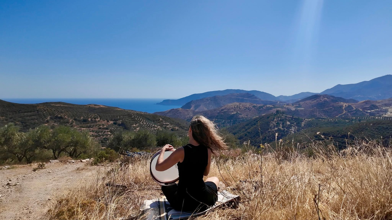 Frame drumming teacher Krista Holland playing her frame drum in Crete overlooking the Aegean Sea.