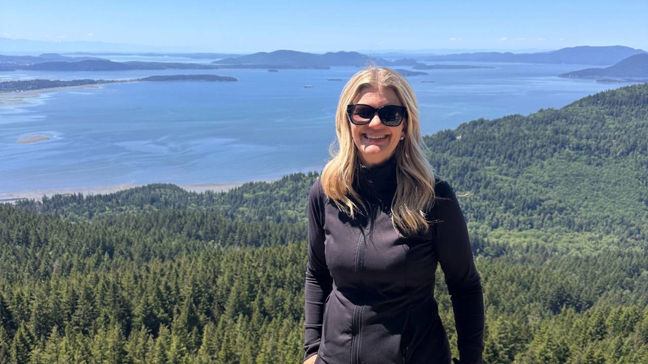 Stacey Salyer smiling at a scenic overlook above a forest and water