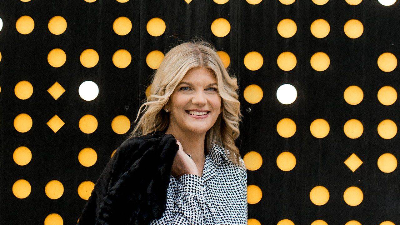 Stacey Salyer smiling in front of a dark wall with amber circles, host of The Stacey Salyer Show
