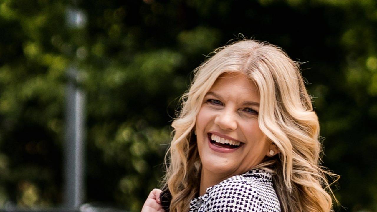 Stacey Salyer laughing while walking confidently down a tree-lined street, glancing back over her shoulder