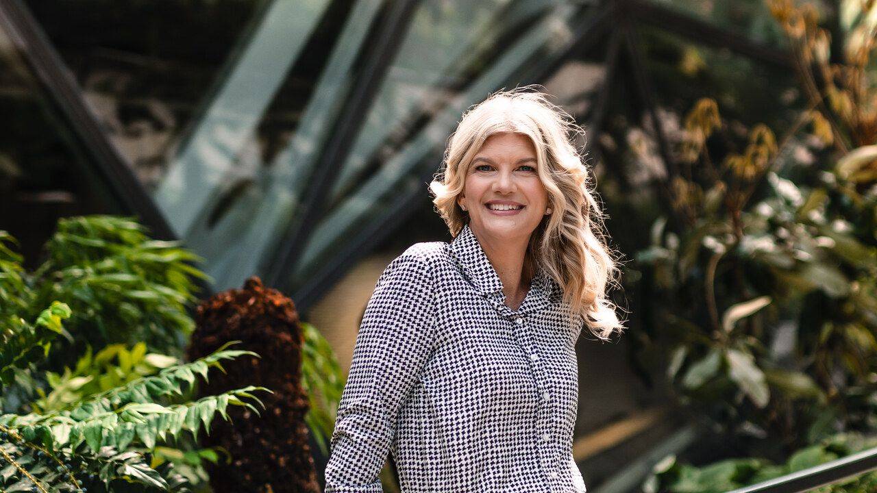 Stacey Salyer smiling in a houndstooth blouse among greenhouse greenery