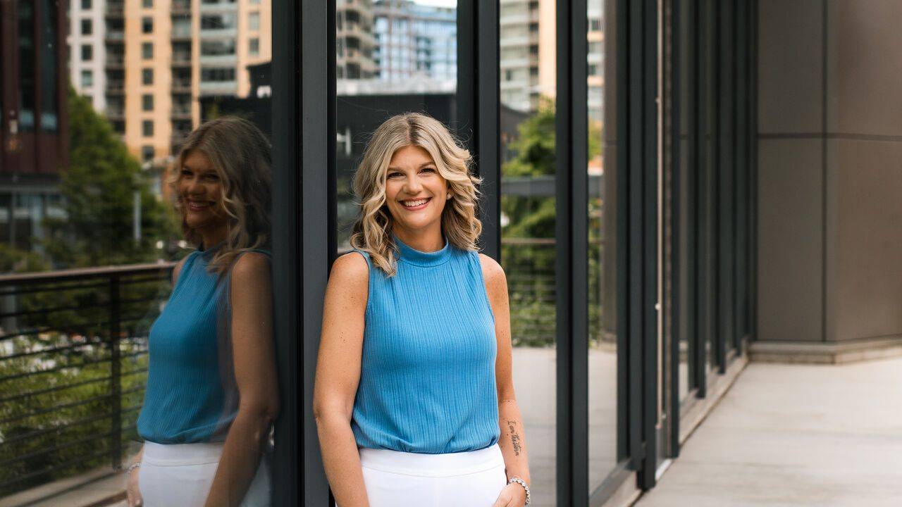 Stacey Salyer standing confidently beside a reflective glass building in the city