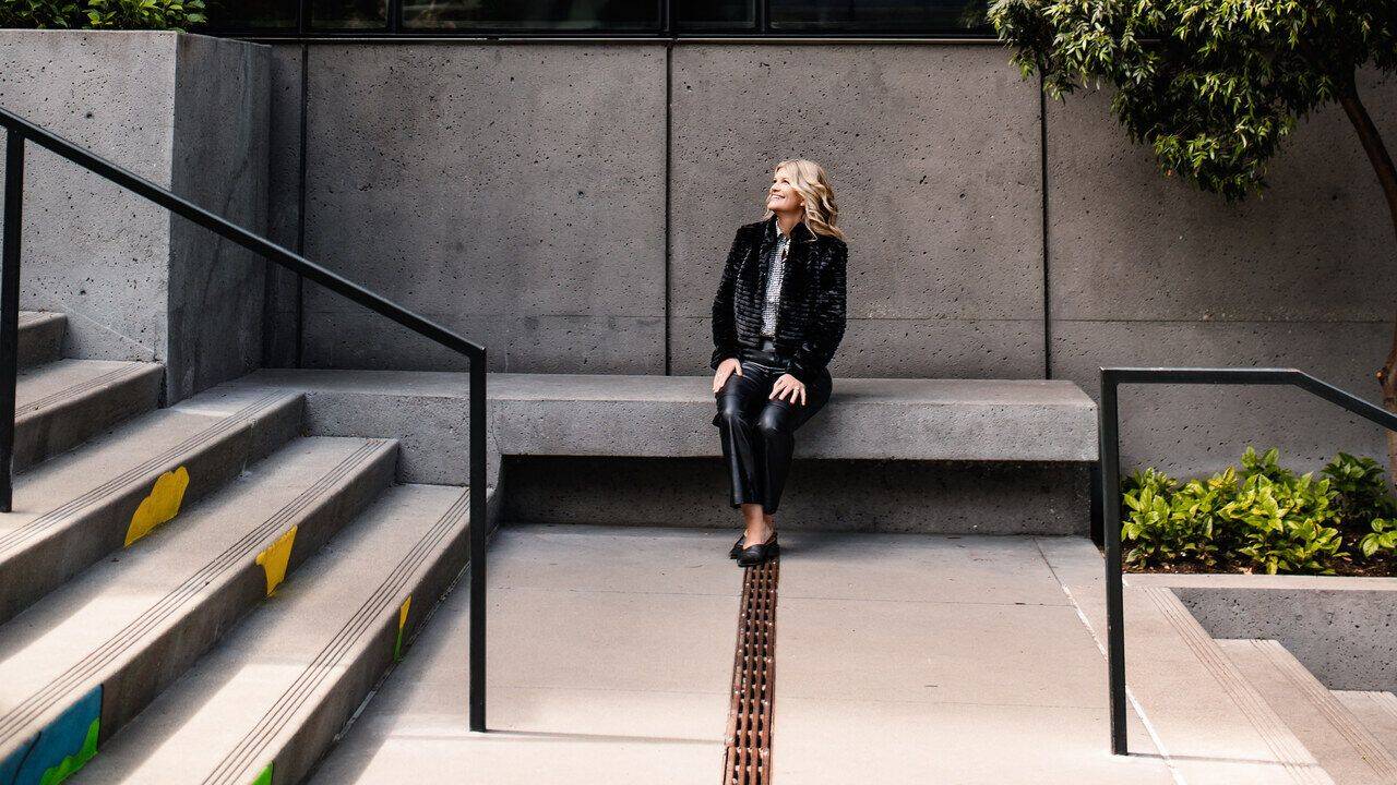Stacey Salyer seated on a city bench looking up thoughtfully
