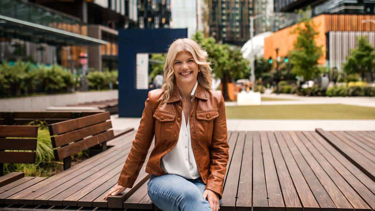 Stacey Salyer smiling, seated on a wooden deck in a city plaza