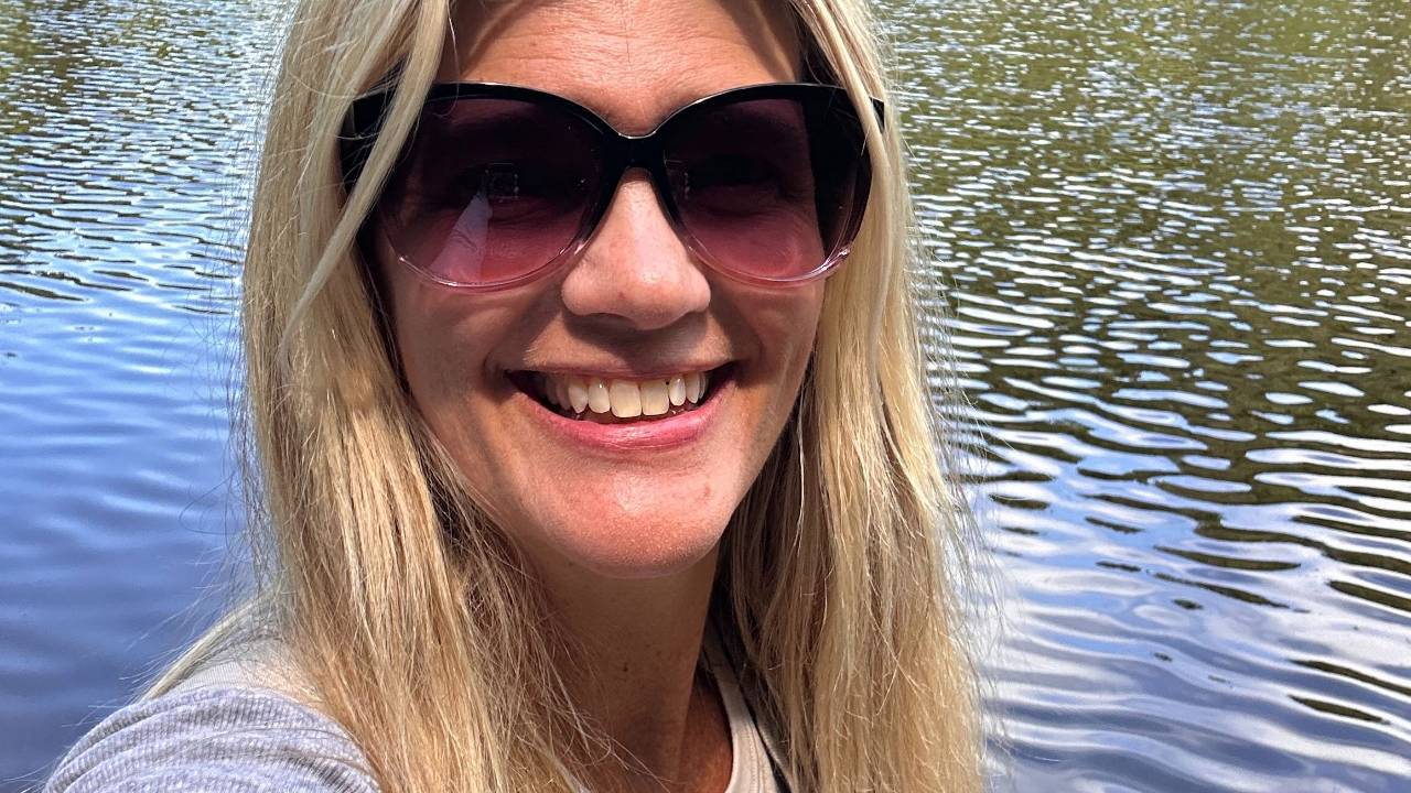 Stacey Salyer smiling in sunglasses beside the water.