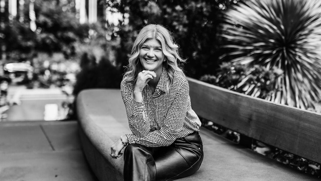Black and white portrait of Stacey Salyer seated on an outdoor bench, smiling