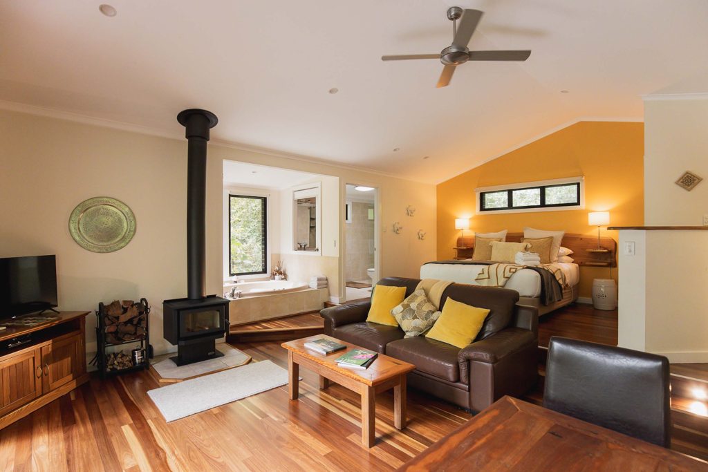 Inside a cabin, a fireplace and a deep bath with rainforest through the window