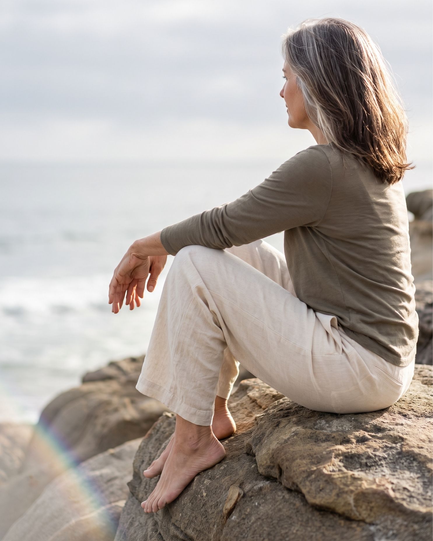 A woman sitting alone above the water, looking out