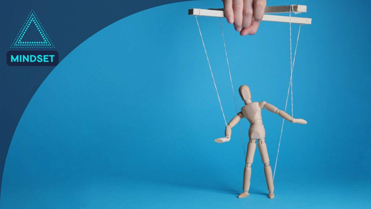 Hand controlling a wooden marionette puppet on strings against a blue background, illustrating the concept of constant influence.