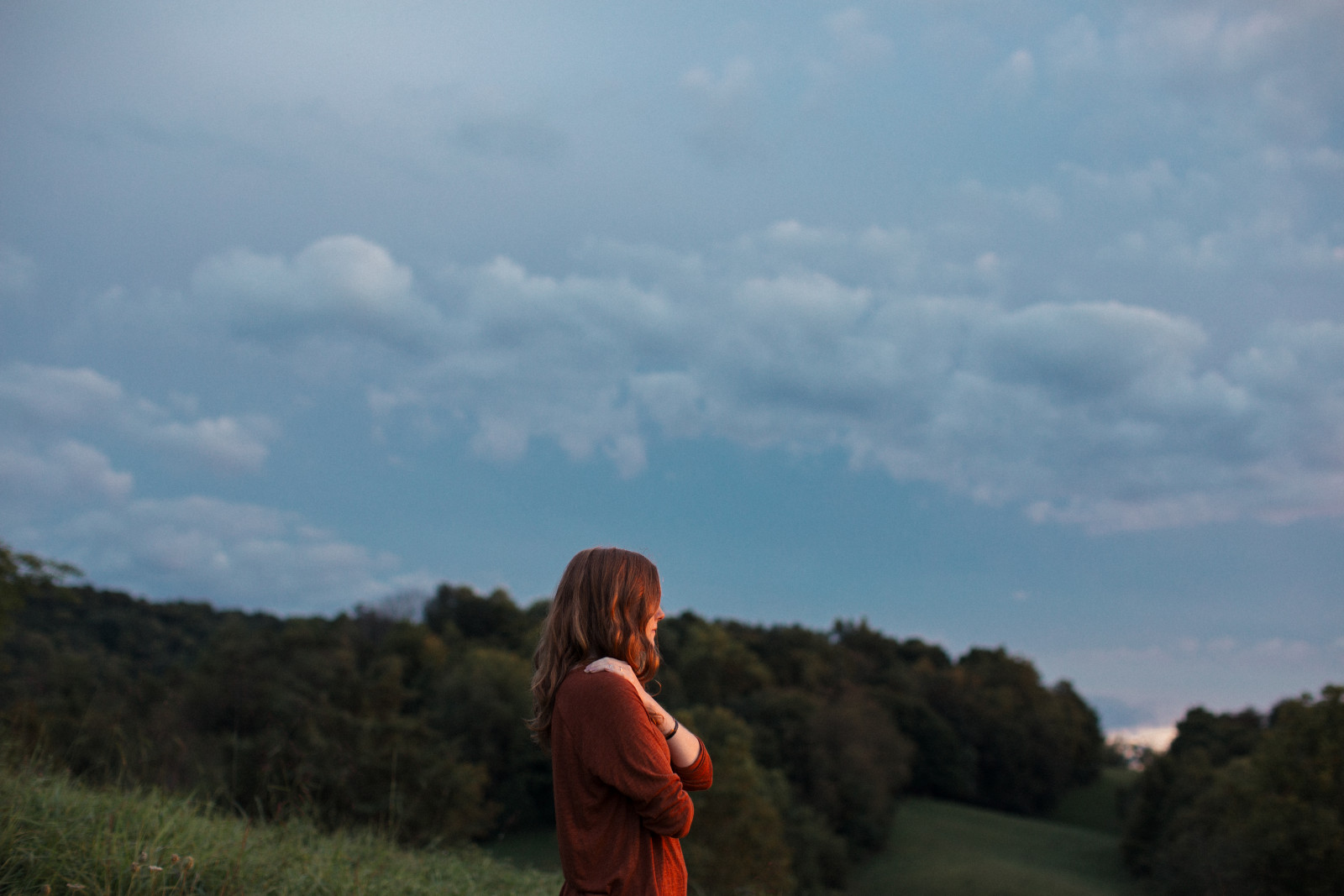 Woman holding herself gently under a dusky sky