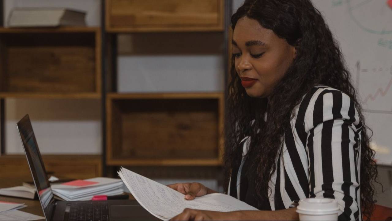 Woman reviewing documents while working on a laptop,researching a coaching business course.