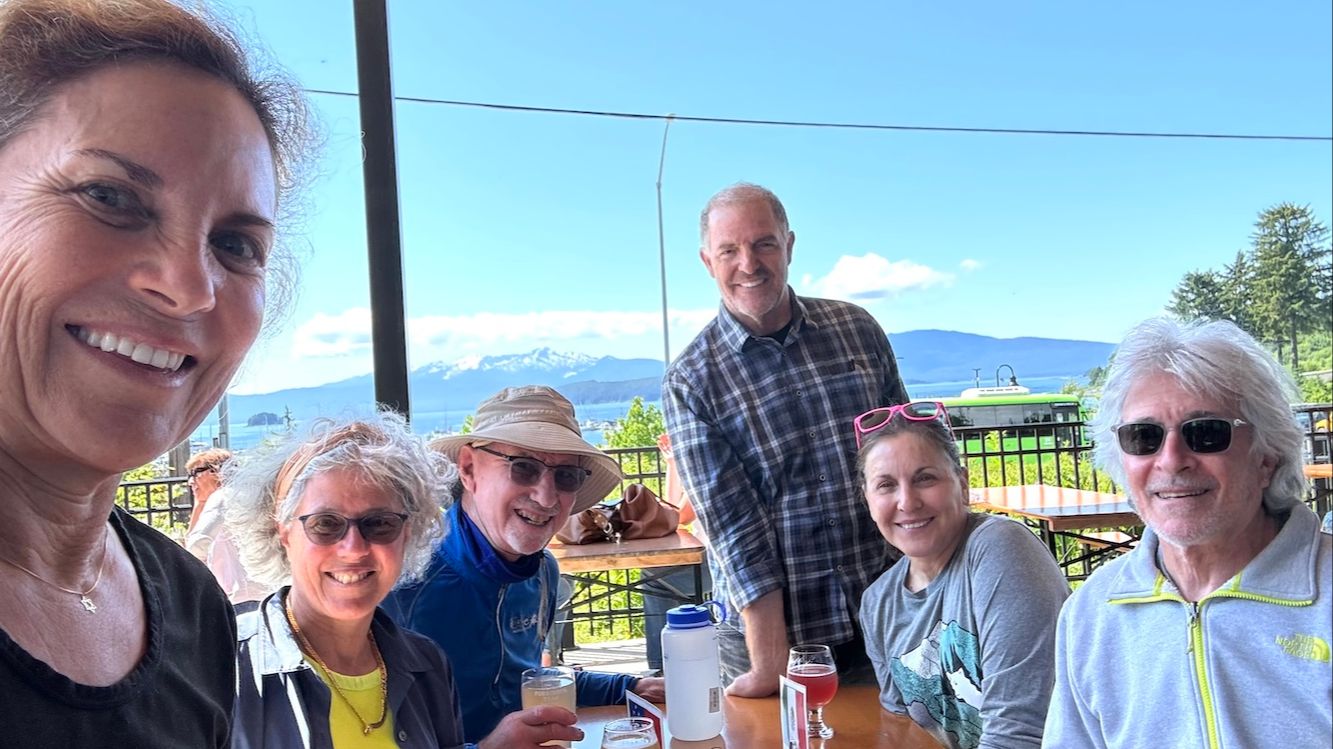 Group of six people at Mendenhall Lake shore with glacier and snow-capped mountains in background, Juneau Alaska