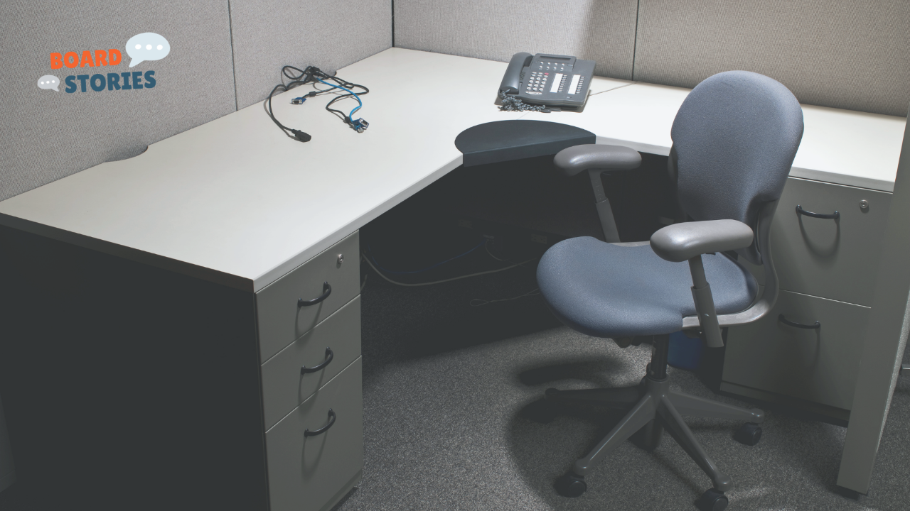 Empty office cubicle with desk chair, phone, and loose cables — no one at the desk.