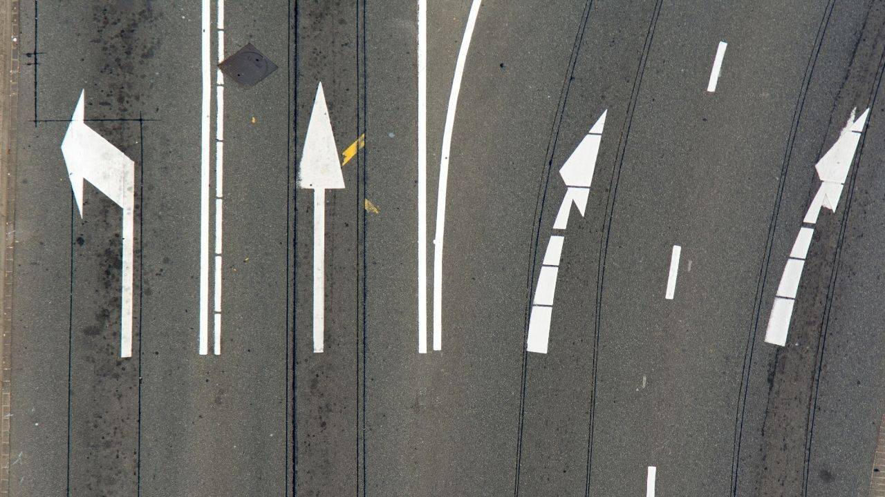 Aerial view of white directional arrows across multiple road lanes, illustrating promotion criteria that keep shifting.