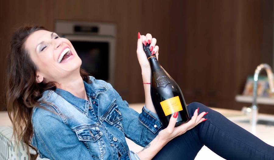 Woman laughing while holding a bottle of champagne, wearing a denim jacket