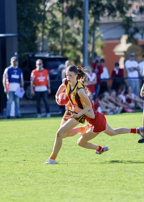 Matilda running with the ball in a junior footy game