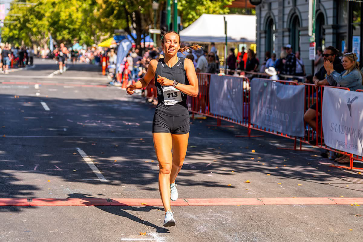 Yaz smiling as she crosses the finish line of a running race