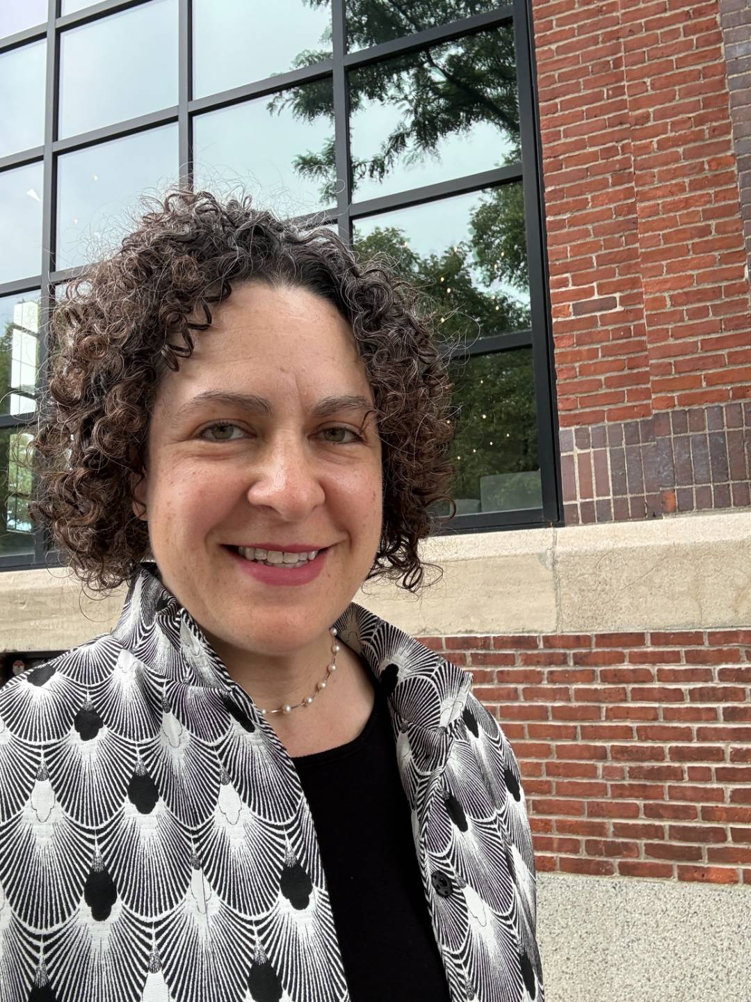 Executive coach and facilitator Erica Mattison wearing a patterned black and white jacket, standing outside the red brick historic Substation building