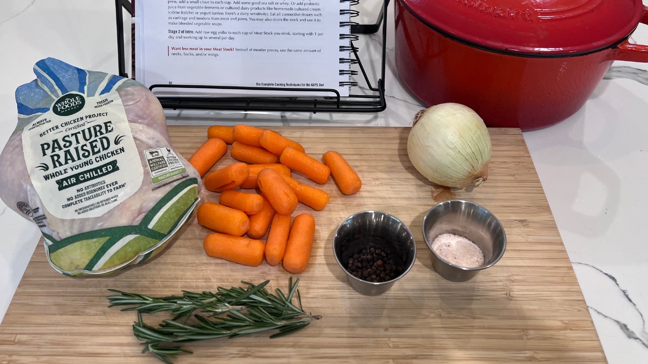 whole chicken, carrots, onion, herbs and spices next to a red dutch oven