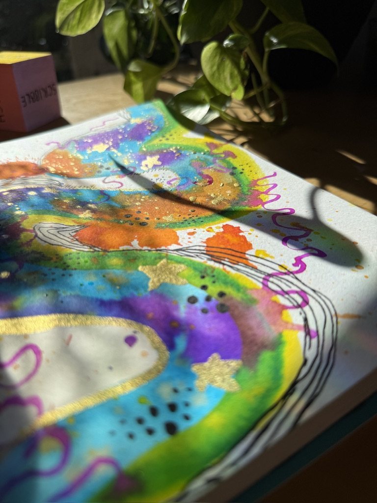 A close-up of rainbow watercolour with gold stars and purple squiggles