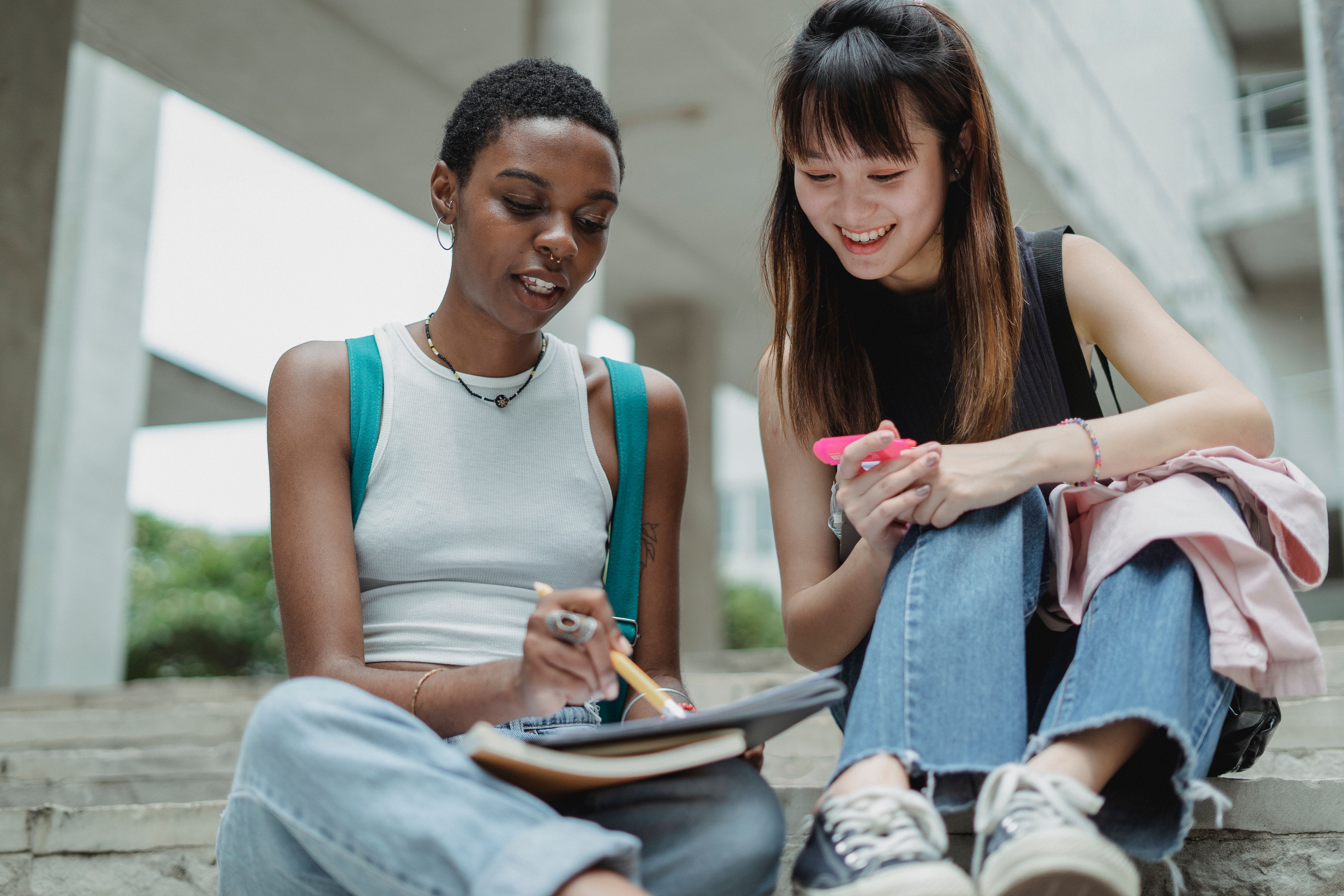 Two students sitting together on campus steps, writing in a planner