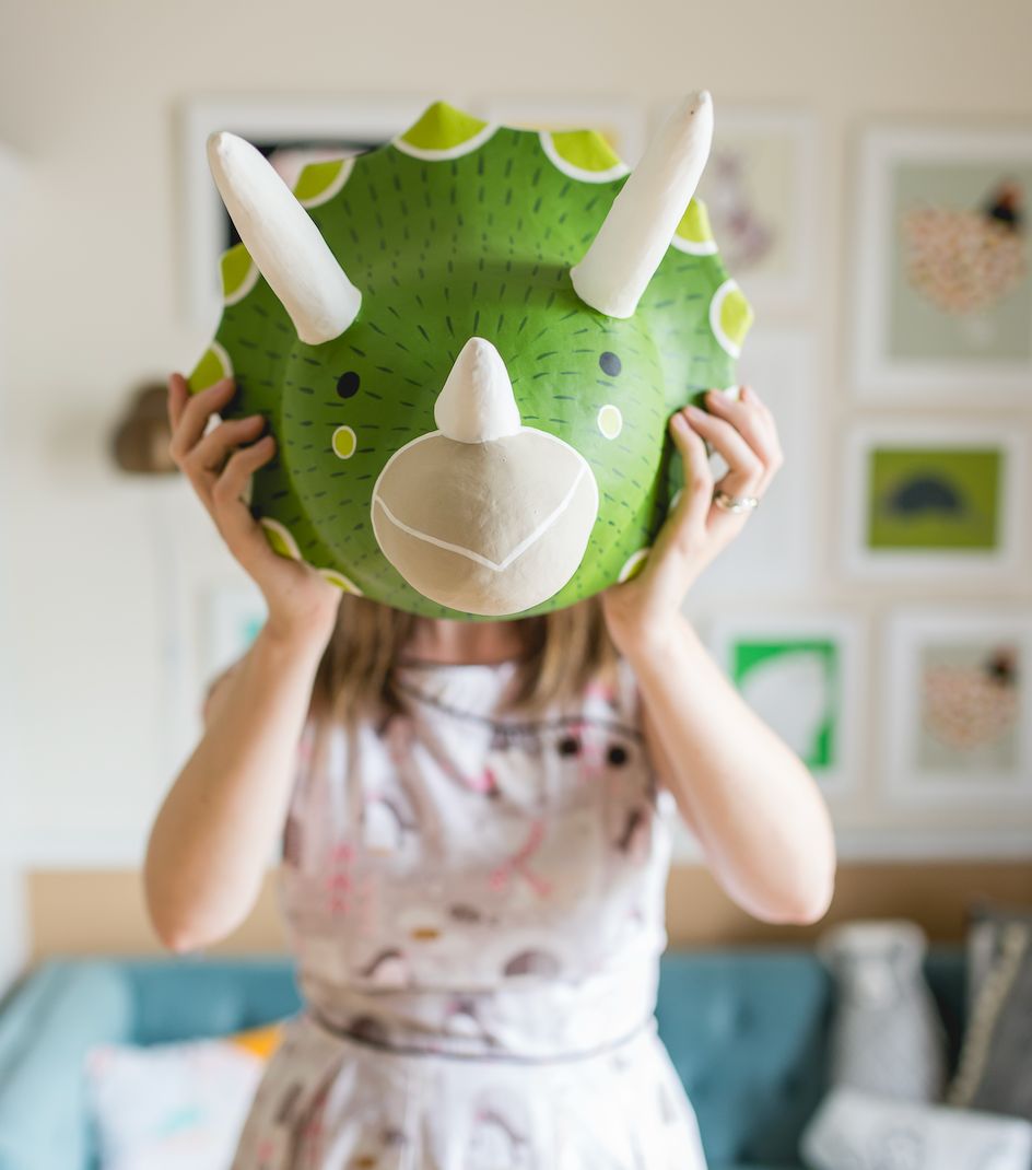 Stacie holding up a hand-painted green triceratops made from her own art
