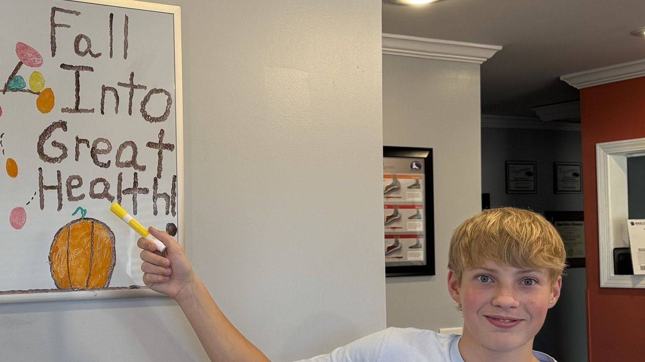 Dr. Dennis's son beside the whiteboard he drew at the BrainCore of Elizabethton front desk, reading Fall Into Great Health