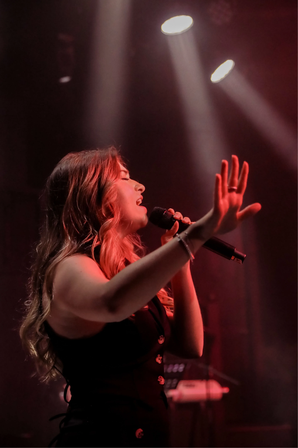 Maestro piano and voice teacher, Katryna, singing live on stage, holding a microphone with red stage lighting