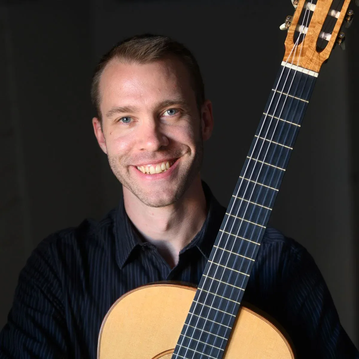 Ben Kunkel, an online guitar teacher, smiles while holding his classical guitar