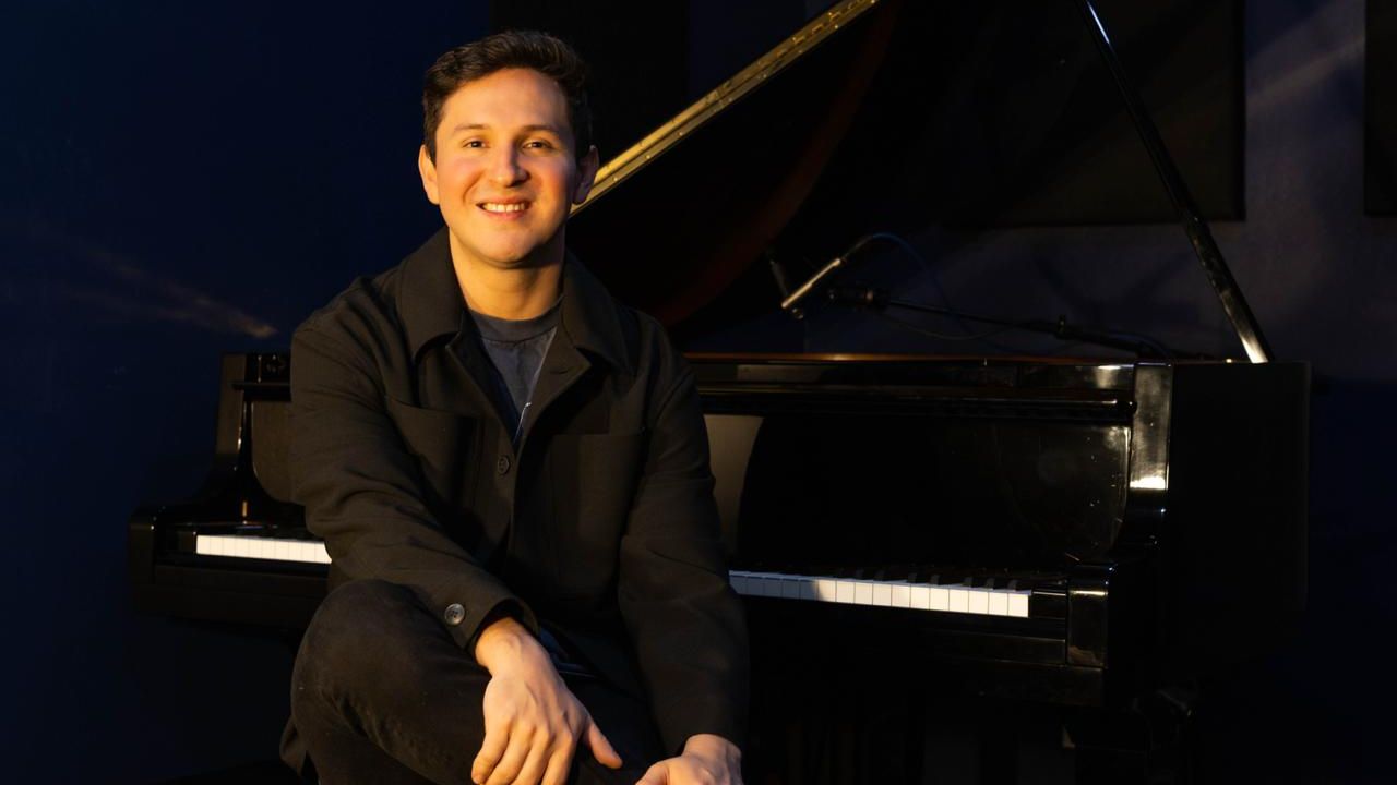 Josue, an online piano teacher at Maestro Music, smiles while seated at a grand piano bench