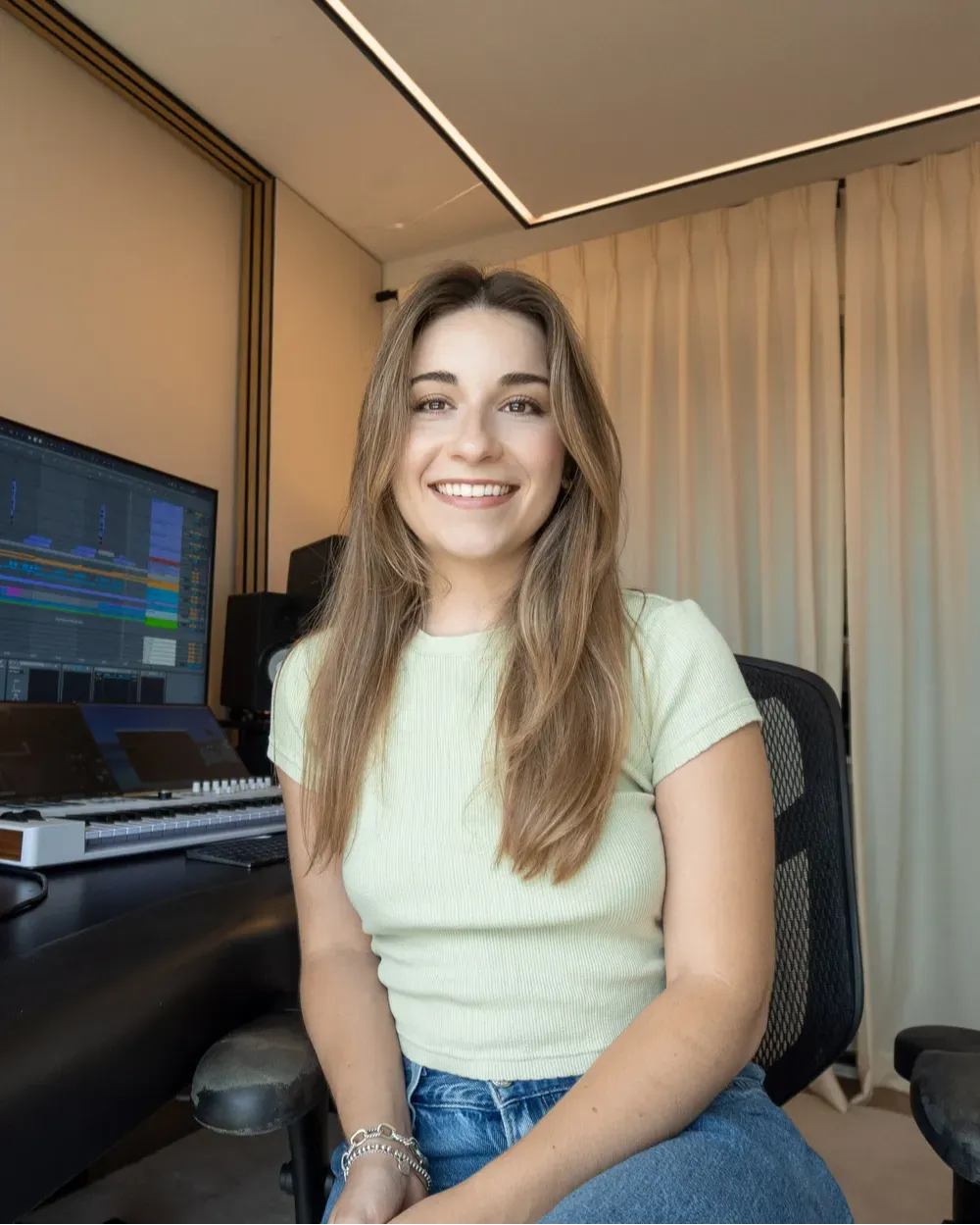 Katryna Marcogliese smiling in front of her desk with audio production and keyboard equipment
