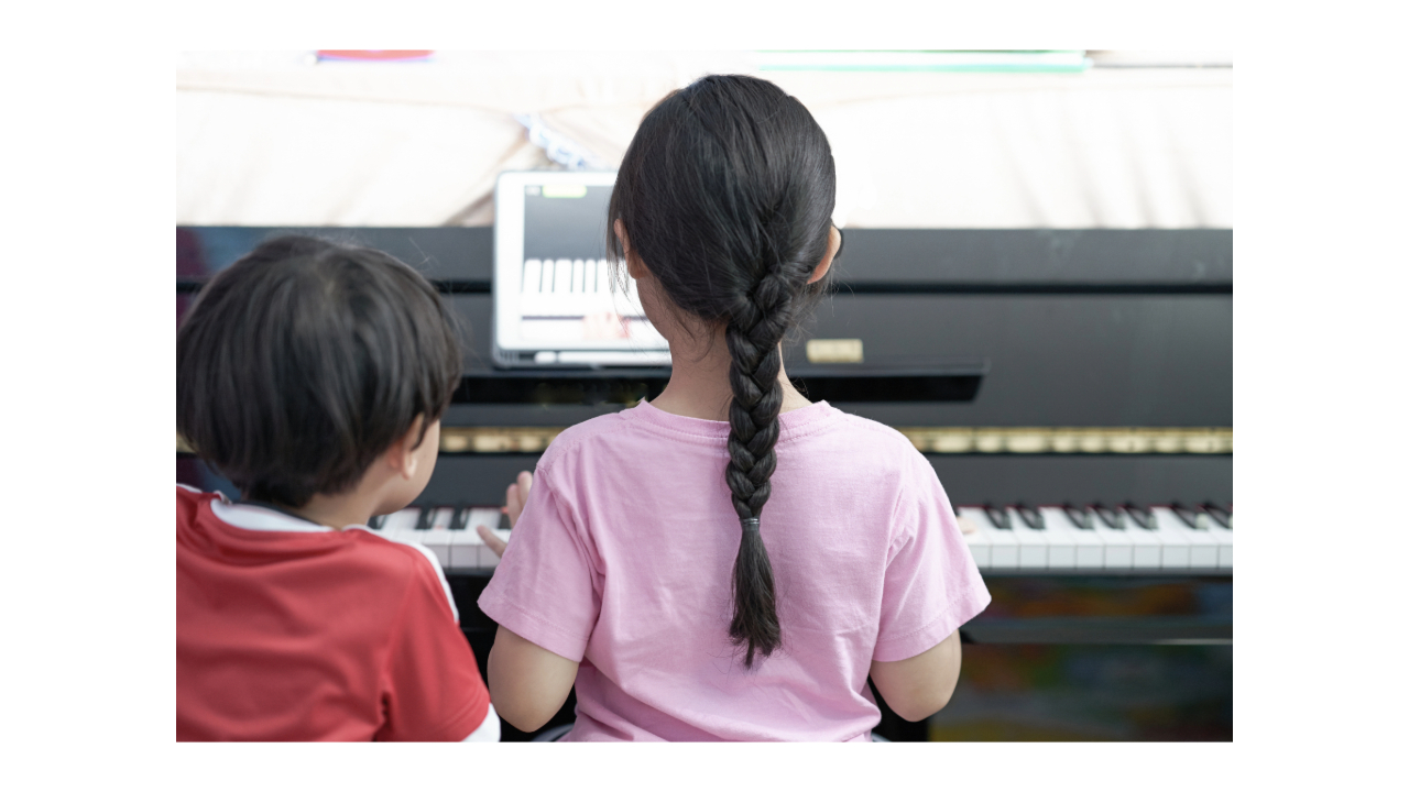 Two children sitting together at a piano during an online music lesson at home
