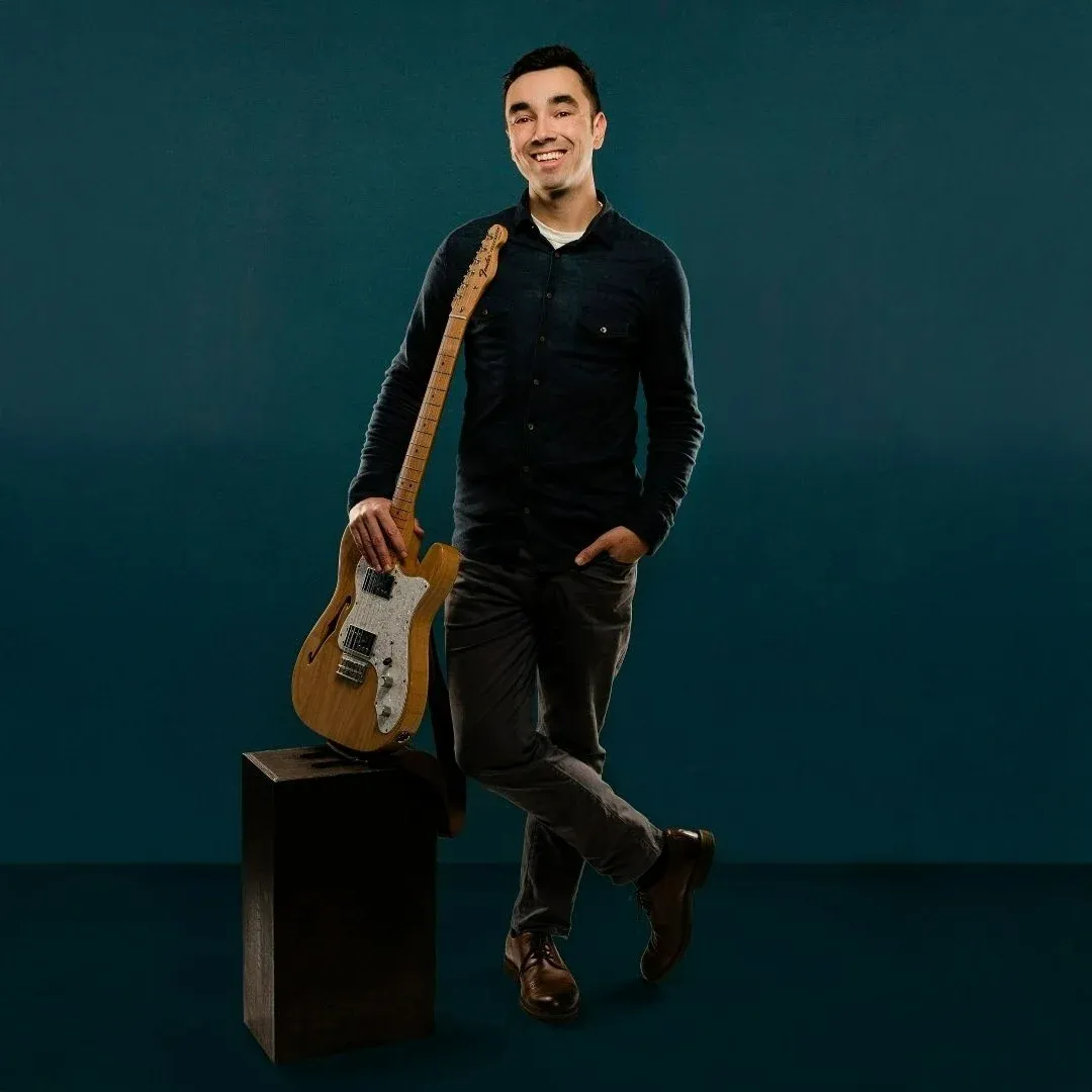 Noah Tretter, music educator and founder of Maestro Music Online, stands smiling with an electric guitar