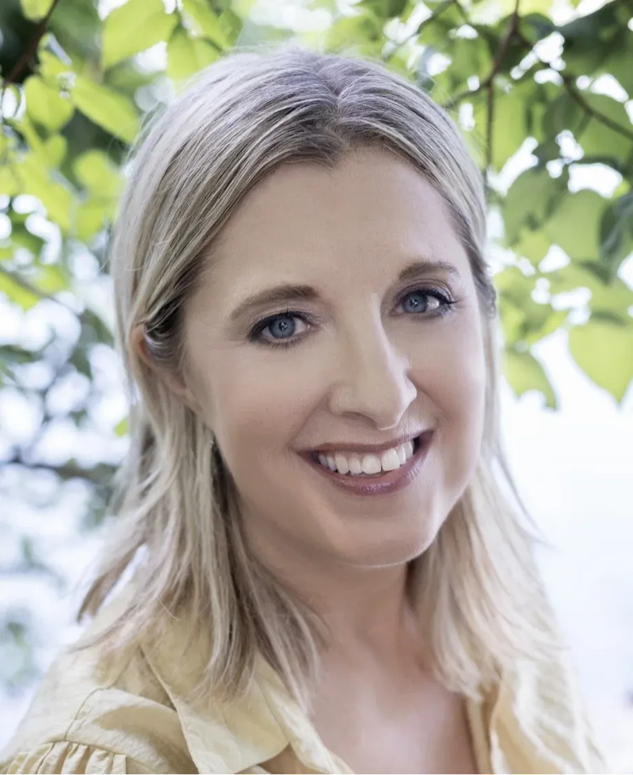 Online piano teacher, Anneliese, smiles at the camera with green leaves in the background