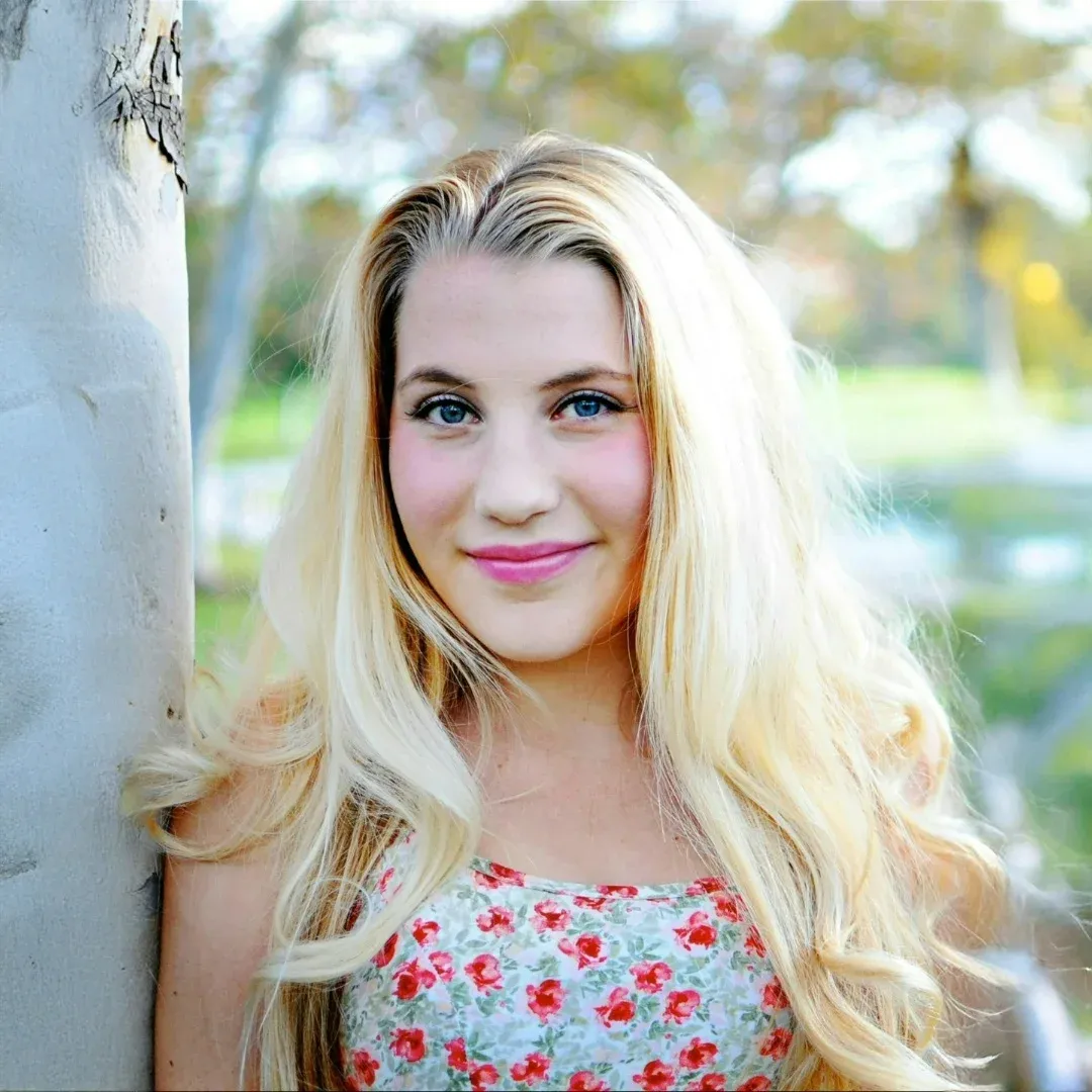 Voice teacher and opera singer, Olivia, smiles while standing next to a tree