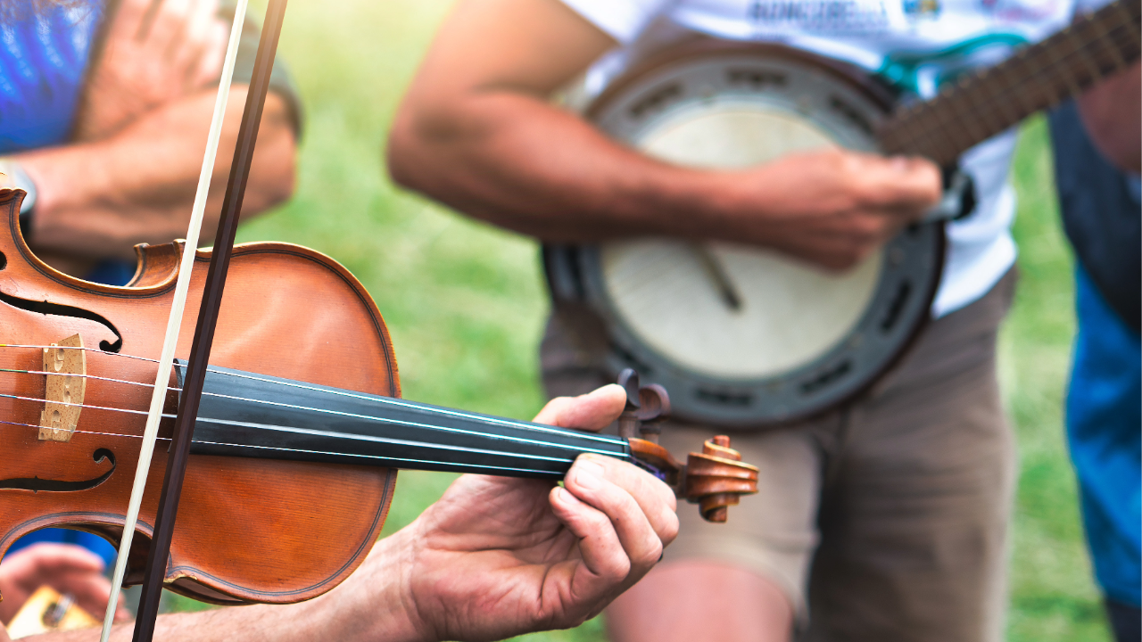 A fiddle and banjo being played together outdoors, representing the folk fiddle tradition.