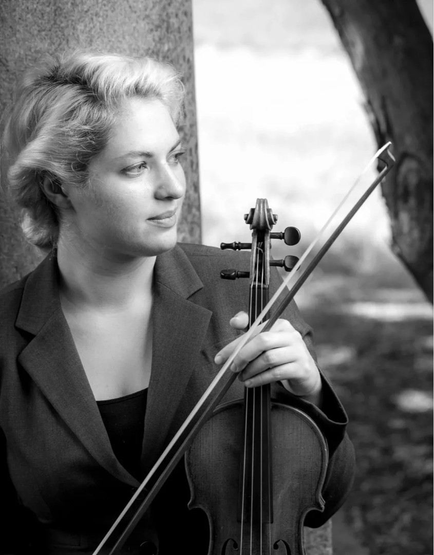 Maestro Music teacher, Melanie Zanakis, in a black-and-white outdoor photo with a violin