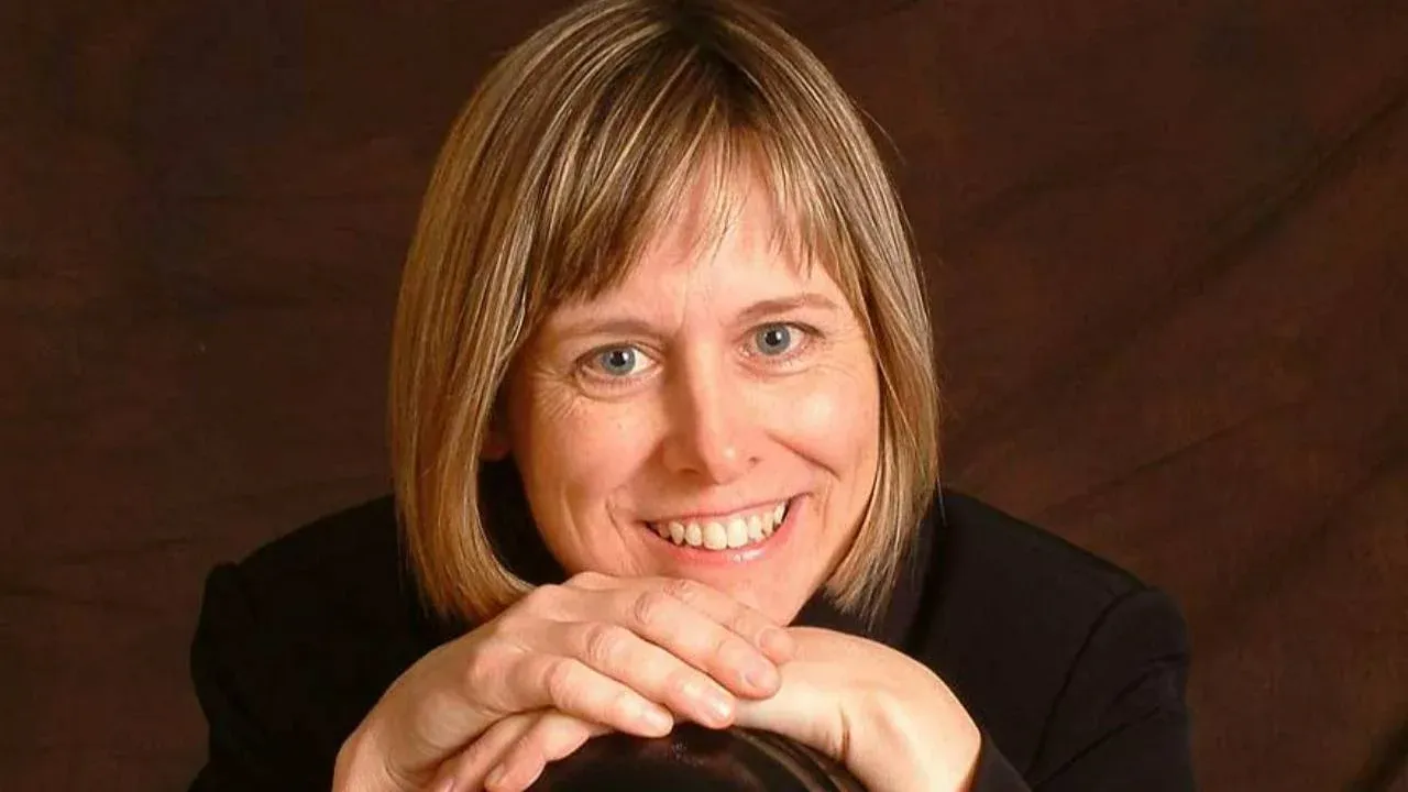 Online piano teacher, Mary, smiles at the camera with a bob haircut and hands resting on a cello case