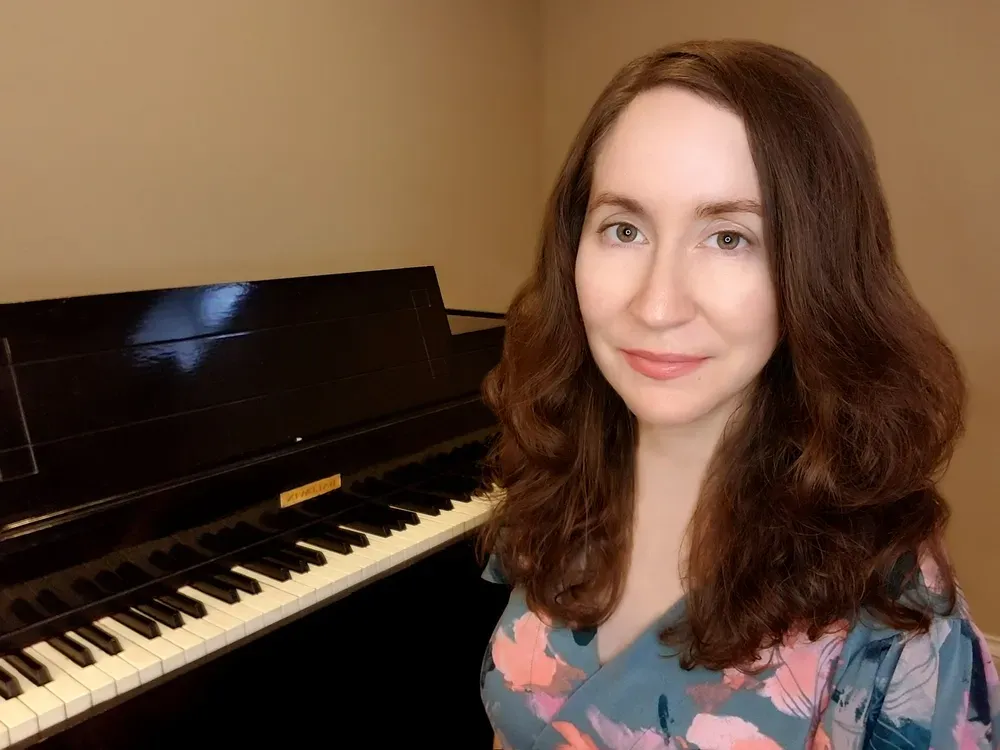 Online piano teacher, Christina, smiles seated in front of a keyboard